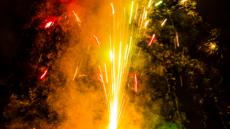 Photo of firecracker erupting in yellow, red, and green sparks.